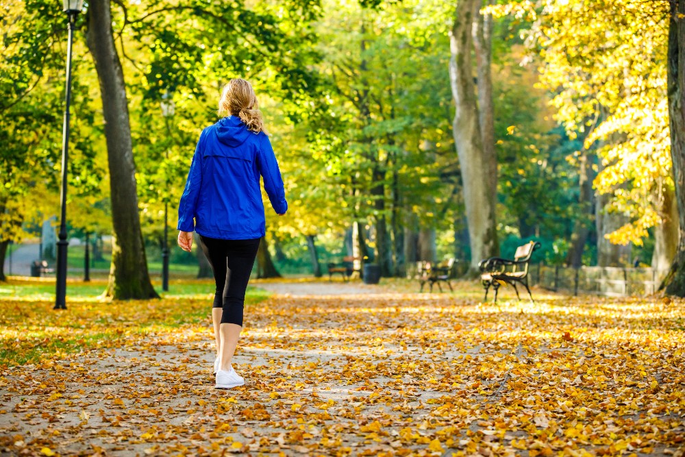 woman walking on a path in a park covered in leaves